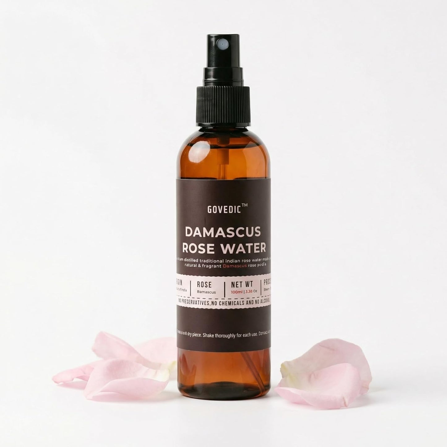 Bottle of Govedic Damascus Rose Water with pink rose petals on a white background